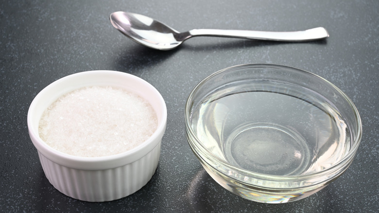 Bir kase şeker ve bir kase su bir kaşıkın yanında oturuyor