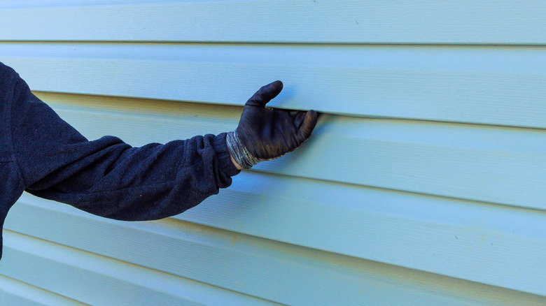 Bir evin siding'ini inceleyen bir kişi