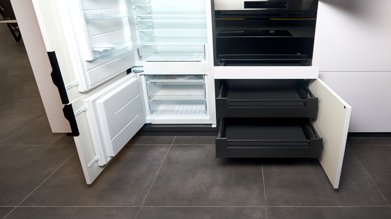 Beyaz mutfak dolabı ve siyah bir fırın arasında entegre bir buzdolabı yer