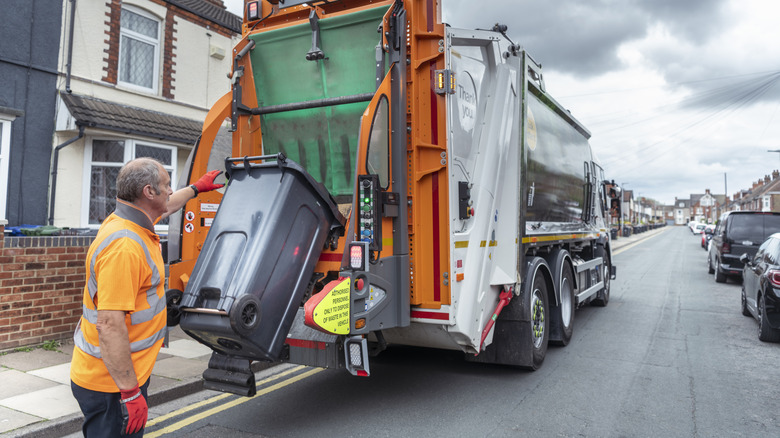 Bir çöp çöp kutusunu arkaya kaldırmak ve dökmek için durdurma çubuğunu kullanan bir çöp kamyonu.