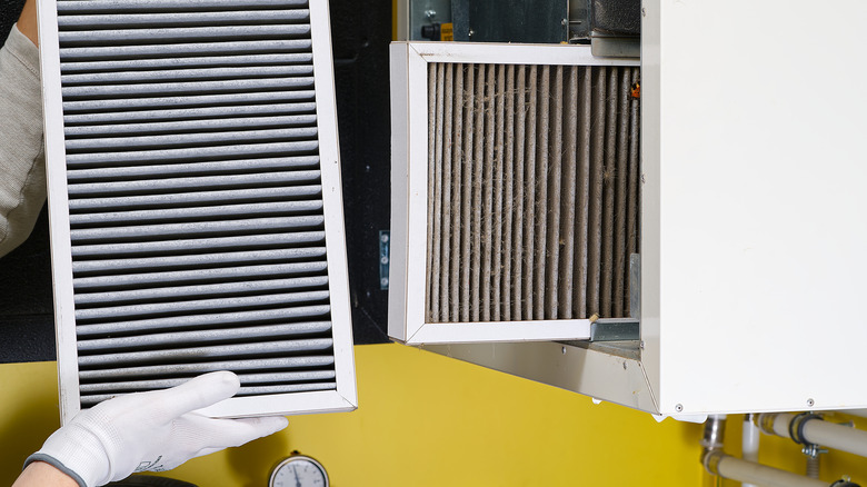 Bir kişi, bir HVAC işleyicisinde kirli bir filtrenin yanında yeni bir hava filtresi tutar