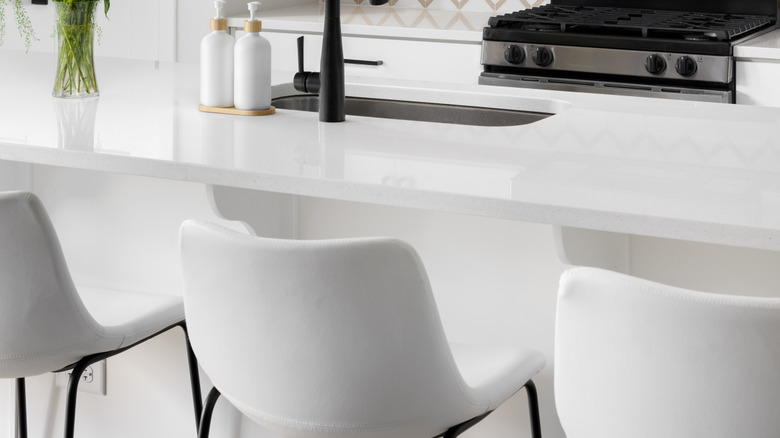 Parlak beyaz bar tabureleri ile modern siyah beyaz bir mutfak.