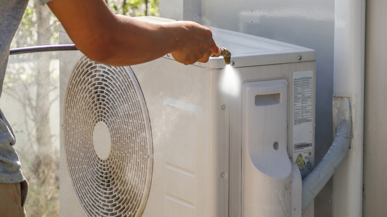Hortum kullanarak bir klima ünitesinin dışını yıkayan bir ev sahibi