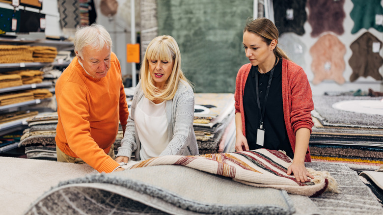 Satış görevlisiyle mağazada satın almak için halıda karar veren kıdemli çift