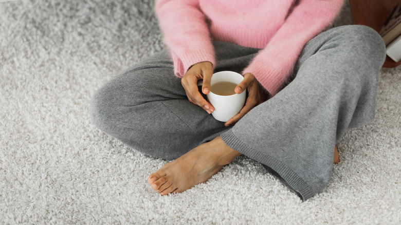 Çay tutarken yün halıda çapraz bacaklı oturan kadın