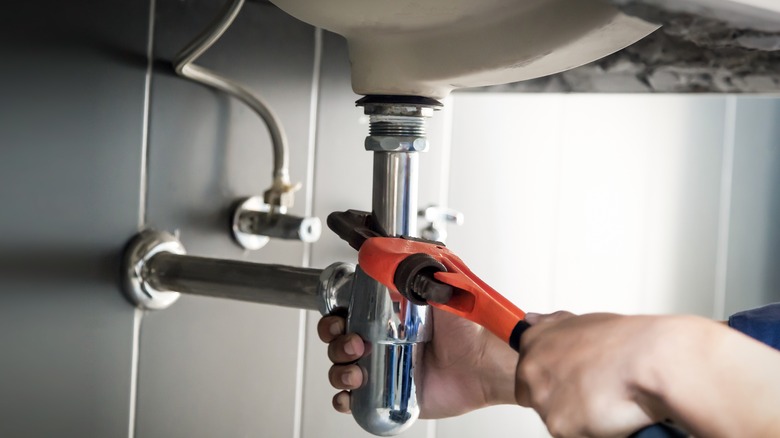 Kişi lavabonun altındaki yeni bir musluğu sıkılaştırır