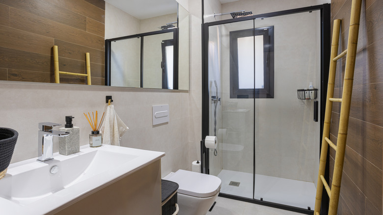 Bir banyoda, önünde bir bambu merdiveni ile siyah metal ile çerçevelenmiş bir duş bulunmaktadır.