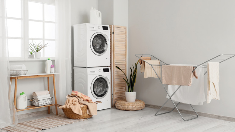 Bir çamaşır odasının köşesinde yığılmış bir çamaşır makinesi ve kurutucu kombinasyonu oturur.