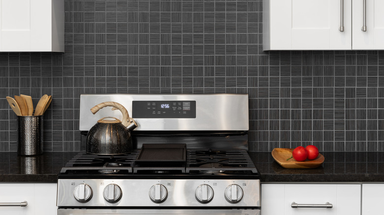 Paslanmaz çelik soba, beyaz dolaplar ve siyah backsplash