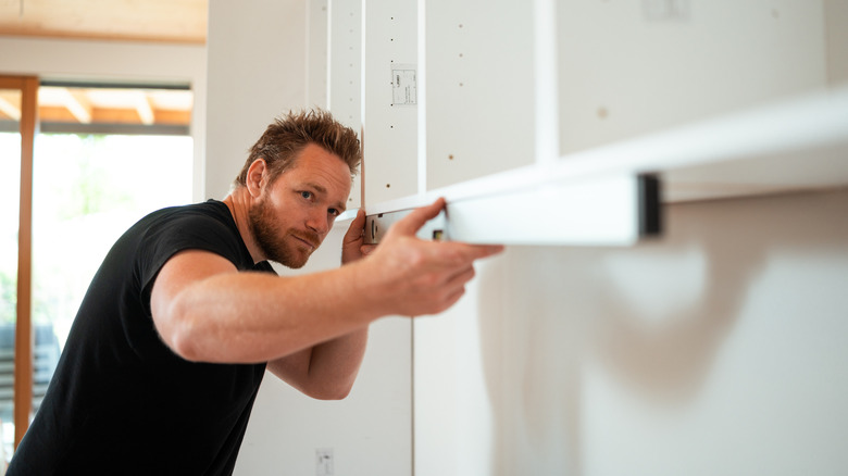 Bir kabinin dibinde bir seviye kullanan adam