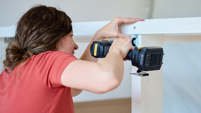 Kablosuz bir matkapla bir mobilya çerçevesi monte eden kadın