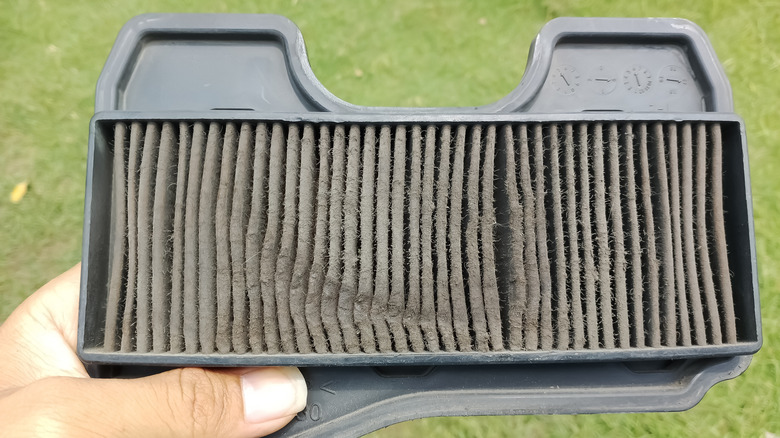 Bir kişi kamera merceğine kadar kirli kağıt çim biçme makinesi hava filtresi tutar.