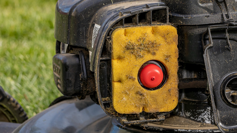 Bir çim biçme makinesi motorunun içinde kirli sarı ve kırmızı köpük hava filtresi.