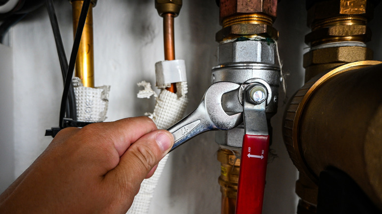 Bir kişi bir anahtar kullanarak bir sıhhi tesisat fikstürünü sıkılaştırır