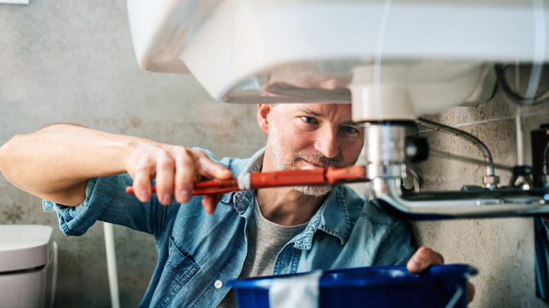 Bir adam bir lavabo altında bir sıhhi tesisat fikstürünü sıkılaştırır