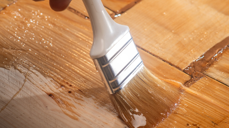 Zımparalanmış ahşap üzerine sıcak tonlu bir leke döşeyen bir boya fırçasının yakın çekim.