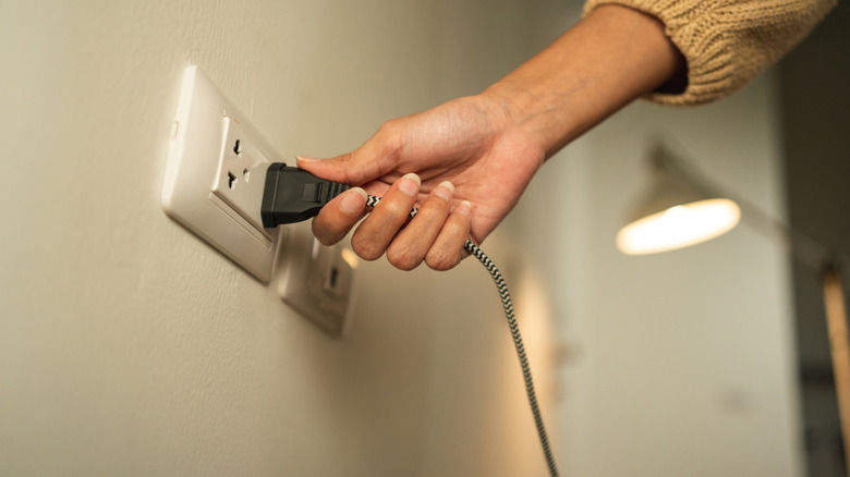 Bir duvar soketine lamba kablosunu takan kişi