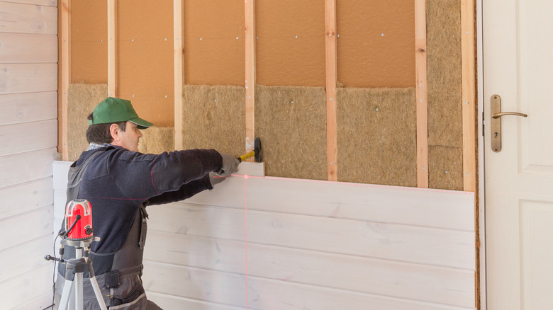 Yarım inşa edilmiş bir duvar çerçevesine doğal elyaf yalıtım ve ahşap panel takan işçi