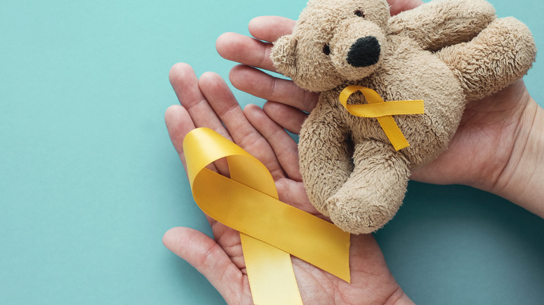 Çocukluk çağı kanseri bilinci için altın şerit ve oyuncak ayı tutan kişi