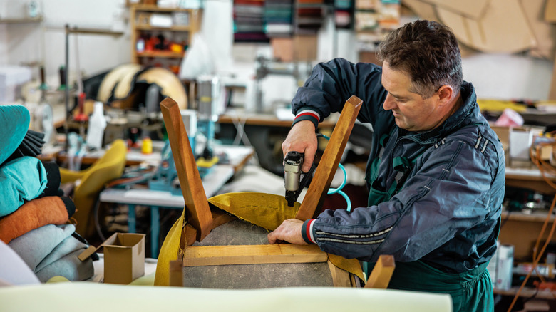 Döşemeli bir sandalyeye kumaşı zımbalanan bir restorasyon uzmanı