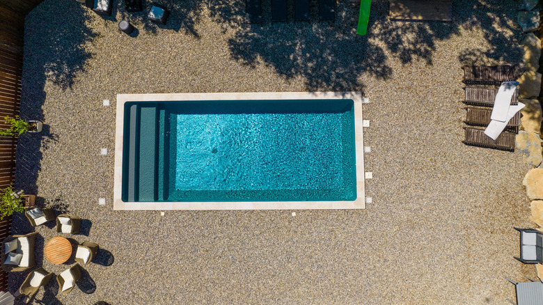 Çakıl ile çevrili dikdörtgen bir yüzme havuzu.