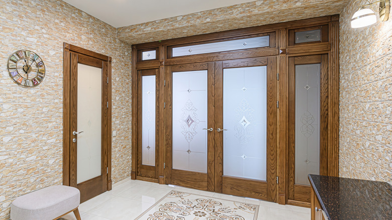 Taş dokulu duvarlar, buzlu cam panelli ahşap kapılar ve desenli bir halı ile iyi aydınlatılmış giriş yolu.