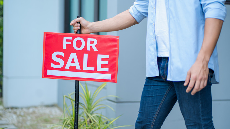 Bir bahçede satılık bir işaret gönderen bir adam.