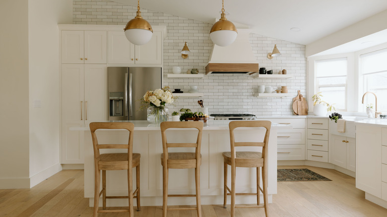 Ahşap bar sandalyeleri, pirinç donanım, backsplash ve ahşap aksan karo ile tamamen beyaz mutfak