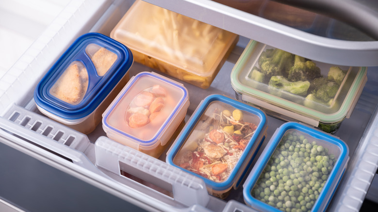 Gıda dolu çok sayıda plastik kap gösteren açık bir dondurucu çekmecesi, düzgün bir şekilde istiflenmiş