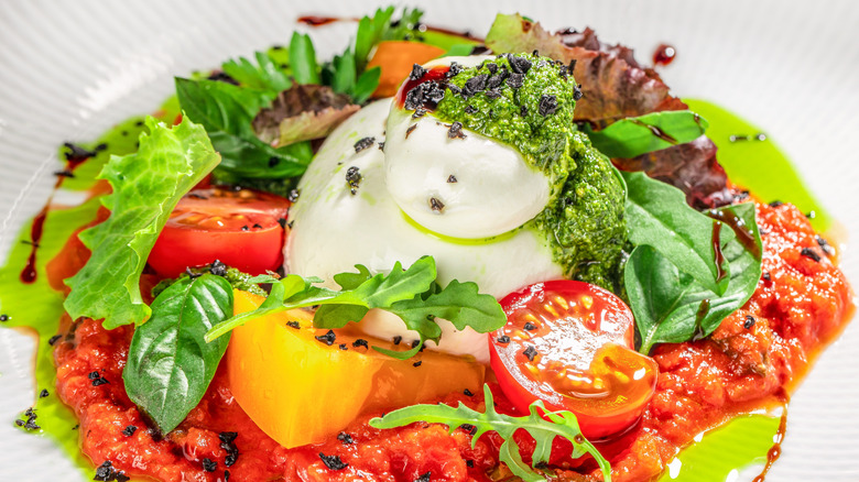 Doğranmış domates, mozzella, yeşillik ve yeşil pesto ile tepesinde domates sosu