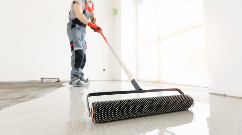 Garajda bir roller ile beton bir zemin takan kişi