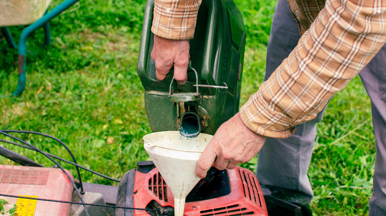 Bir adam çim biçme makinesini benzinle doldurur
