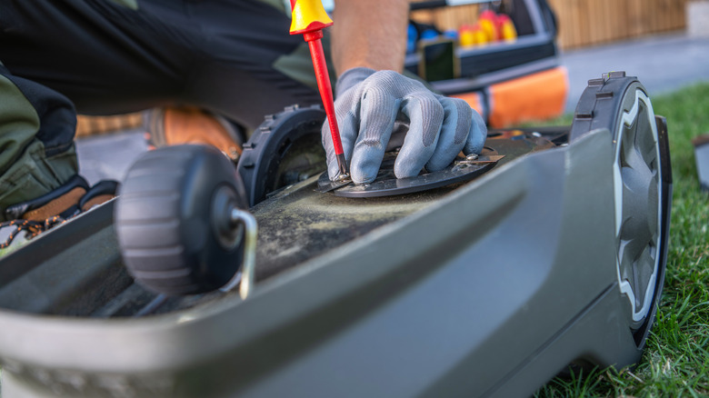 Bir kişi bir çim biçme makinesi üzerinde bazı bakım işi yapıyor