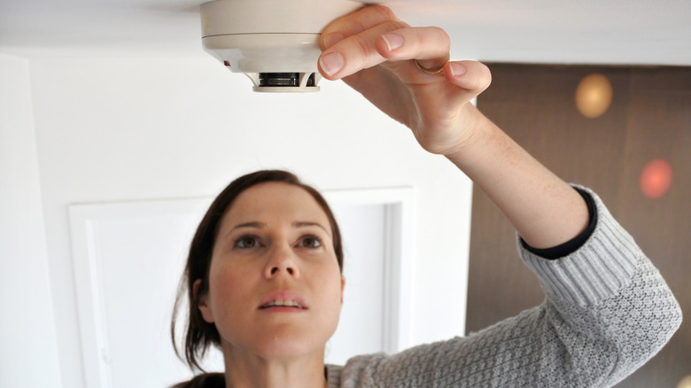 Tavanda duman dedektörünü kontrol eden kadın