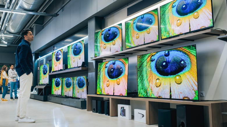 Yüksek kaliteli çözünürlüklü ekranlara ve canlı renk iletimine sahip çeşitli modern akıllı TV setlerine bakan bir kişi