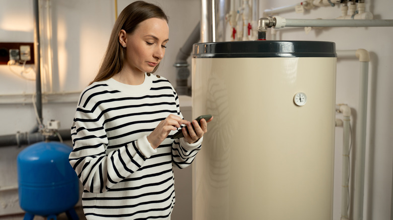 Bir su ısıtıcısını inceleyen ve telefonunda not alan bir kadın
