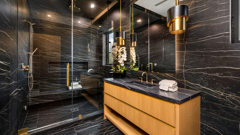 Ahşap dolap ve altın aksanlı duvarlar, zeminler ve tezgahta siyah mermer modern banyo