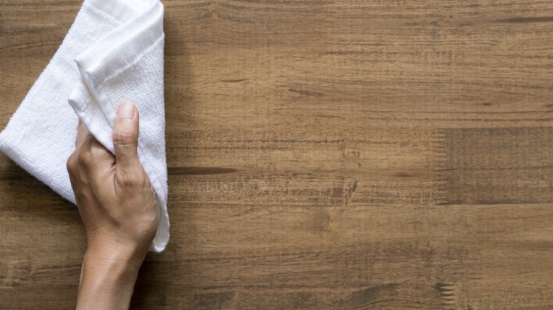 Bir ahşap yüzeyi beyaz bir bezle temizleyen bir el.
