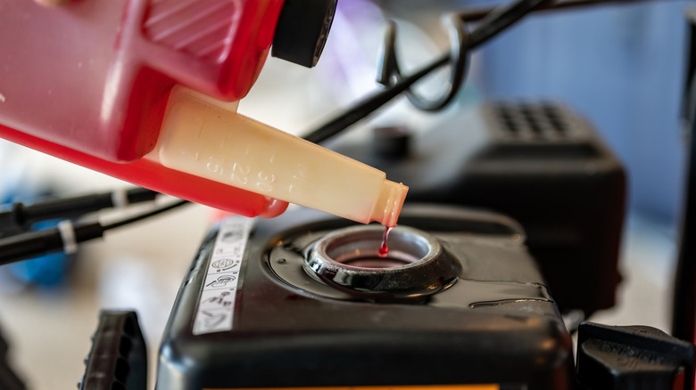 Bir çim biçme makinesi gaz tankına yakıt dengeleyici ekleyen bir kişi