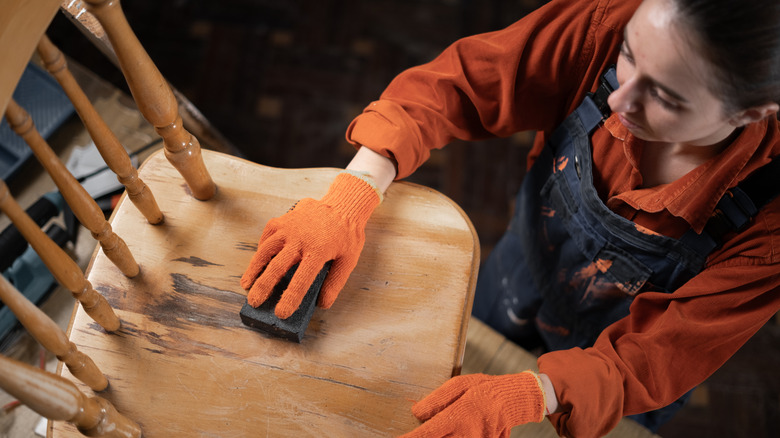 Ahşap bir sandalyenin koltuğunu zımparalayan bir kadın