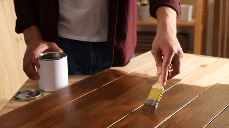 Bir kişi ahşap yüzeye koyu leke uygular