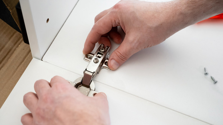 Bir kabinin altına bir menteşe takan kişi