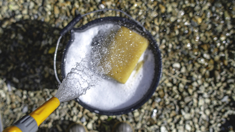 çakıl taşları yıkamak için sabunlu bir kovaya su döken bir hortum