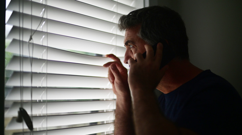 Telefonda panjurlarından bakan bir adam.