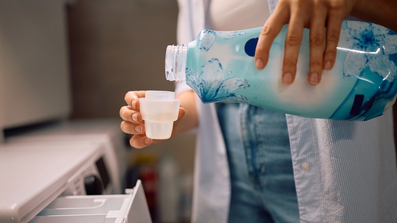 Çamaşır odasında çamaşır makinesinde kullanmak için kumaş yumuşatıcı döken kadının yakın çekimi, çamaşır rutininde ortak bir adım vurgulayın.