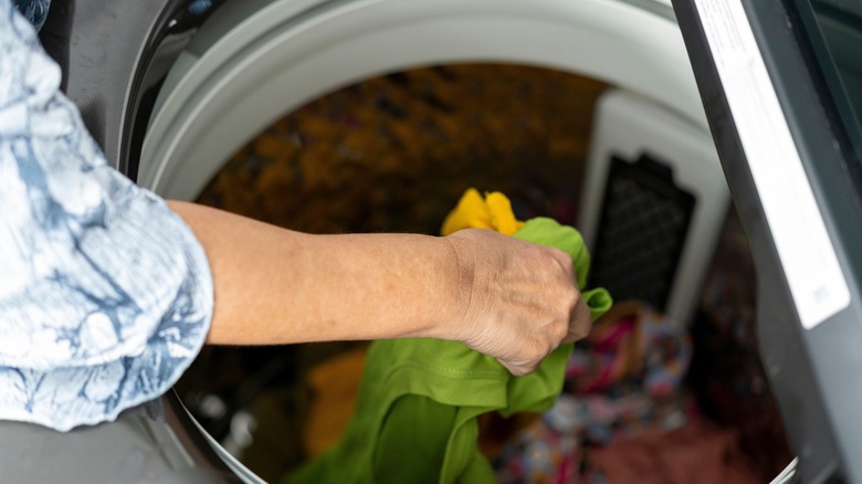 Üst düzey bir kadının eli çamaşır makinesine çamaşır makinesine yükleyen bir el.