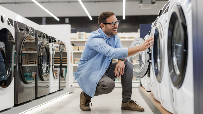 Gülümseyen bir adam, bir cihaz mağazasında modern çamaşır makinelerini inceler.
