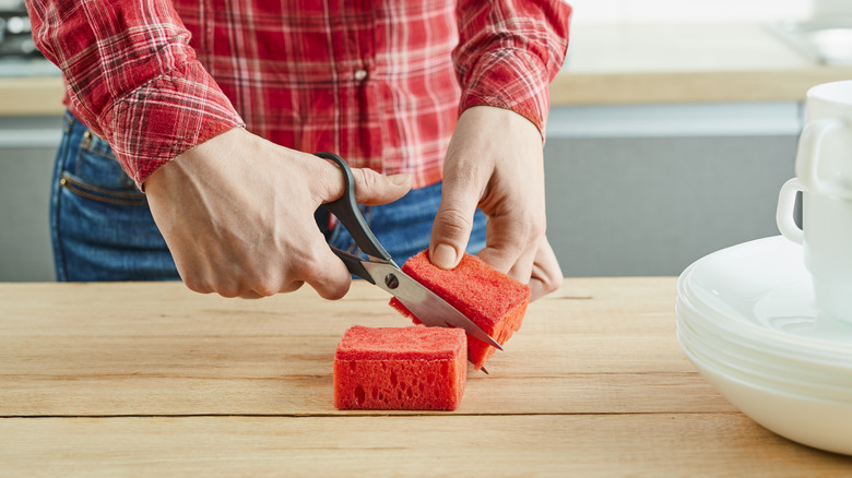 Kırmızı mutfak süngerini makasla kesen bir kişi
