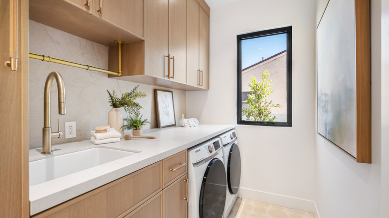 Depolama için havai dolaplar, çekmeceler ve taban dolapları ile pirinç donanımlı bir lavabo, yıkayıcı ve kurutucu ile çamaşır ve yardımcı oda