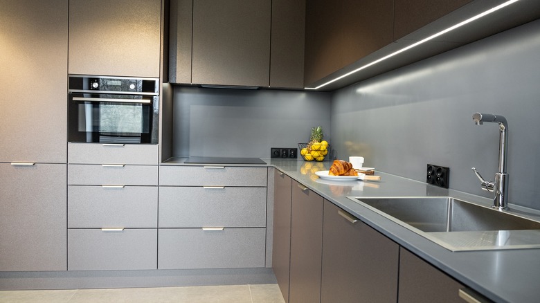 Dolapların altında doğrusal aydınlatma ve şık, düz gri bir backsplash olan modern bir mutfak.